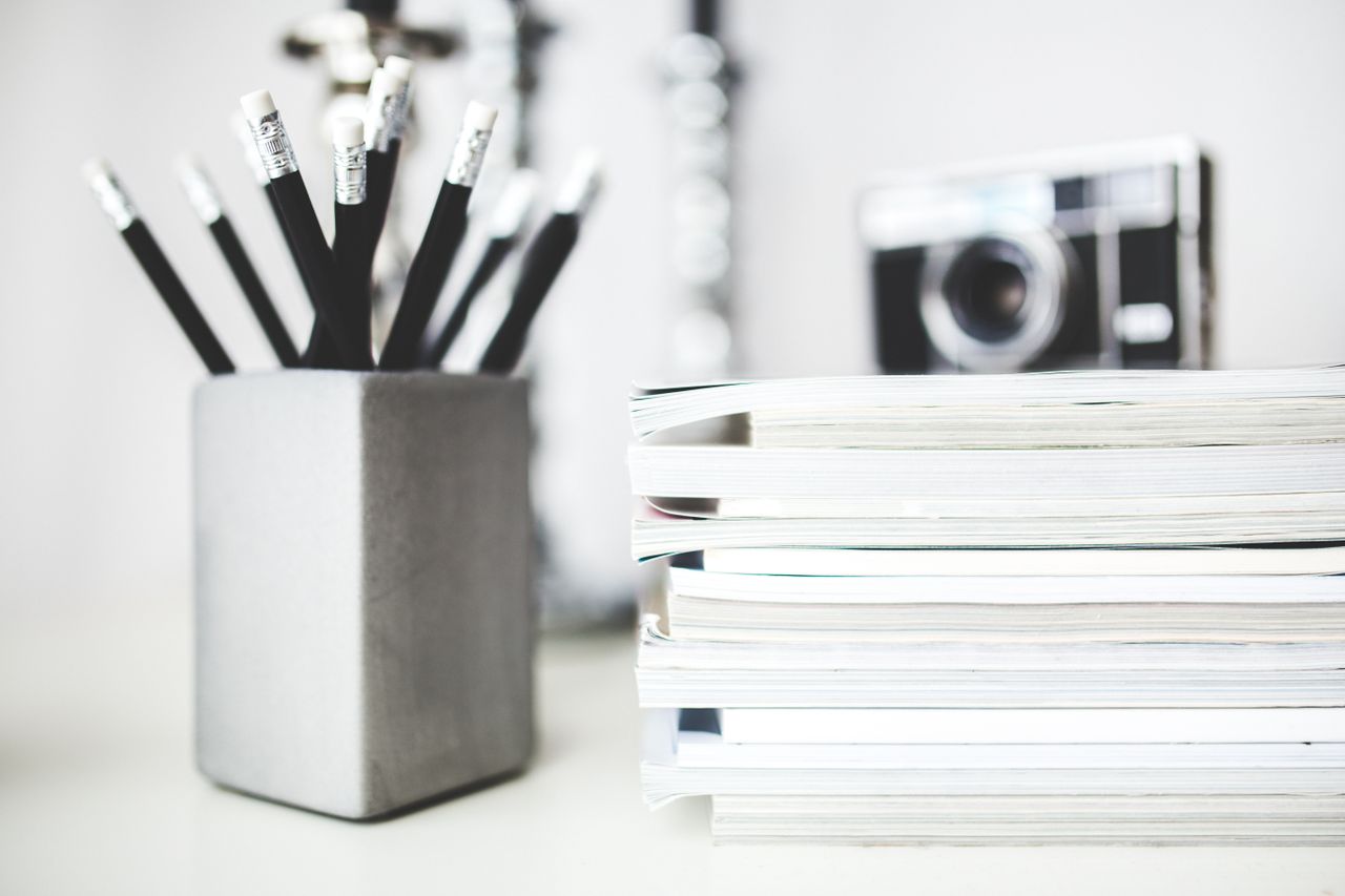 Organized workspace featuring pencils in holder and stacked magazines with a vintage camera in the background.