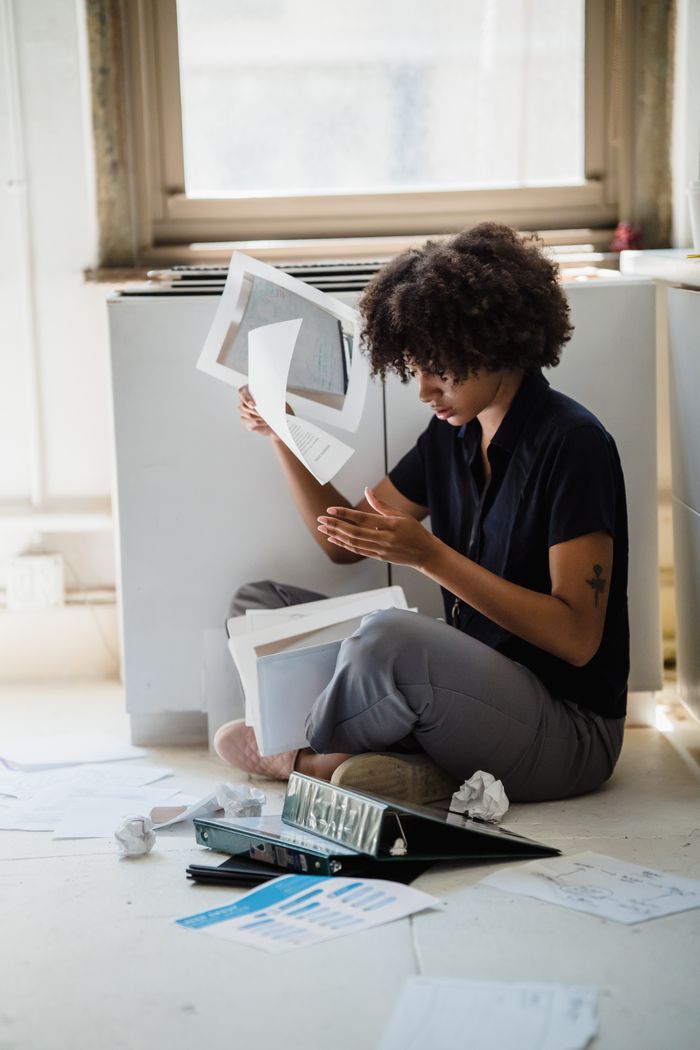 Woman sitting on the floor sorting papers and documents in an office setting.