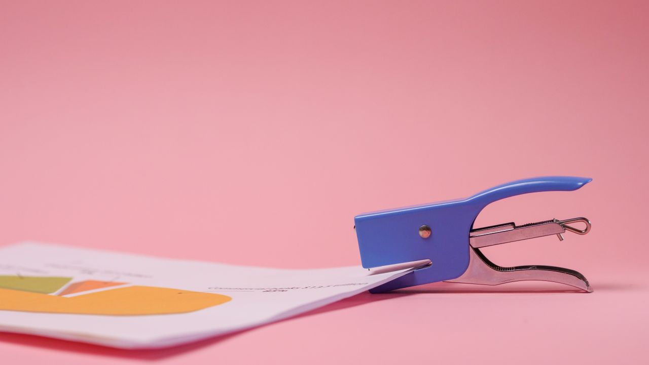 A blue stapler securing colorful papers against a vibrant pink backdrop.